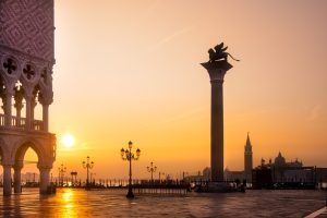 Alba dorata su Piazza San Marco a Venezia: vista con la Colonna del Leone di San Marco, Palazzo Ducale e il Campanile sullo sfondo, un'ispirazione per cosa vedere.
