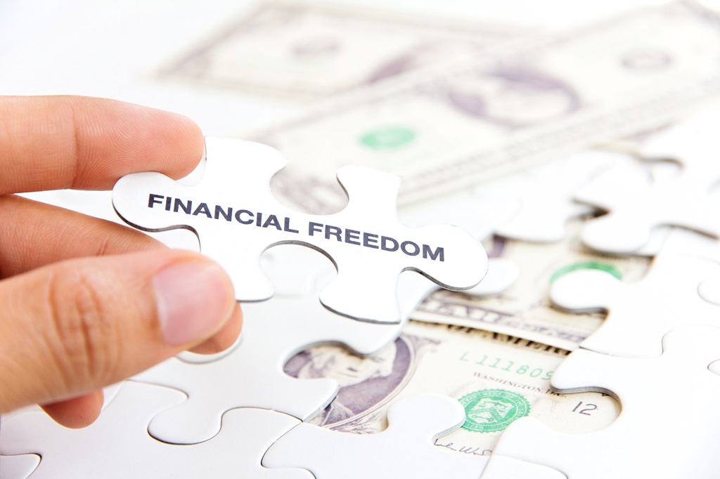 Mano che completa un puzzle con il pezzo 'Financial Freedom', simbolo della guida alla libertà finanziaria, su sfondo di banconote.