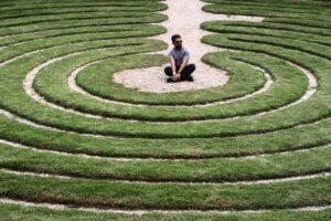 Un uomo seduto al centro di un labirinto a spirale nell'erba: rappresenta la cecità esperienziale e la gabbia delle conoscenze descritte dal modello S.I.R.E.