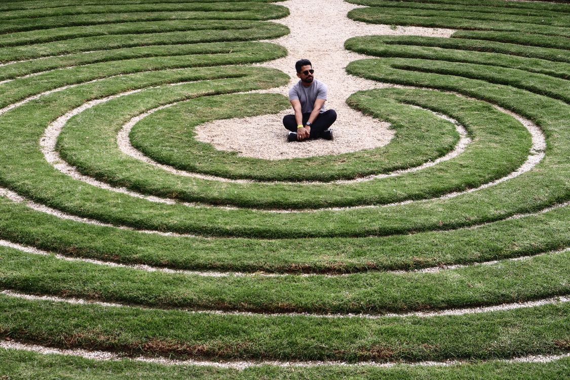 Un uomo seduto al centro di un labirinto a spirale nell'erba: rappresenta la cecità esperienziale e la gabbia delle conoscenze descritte dal modello S.I.R.E.