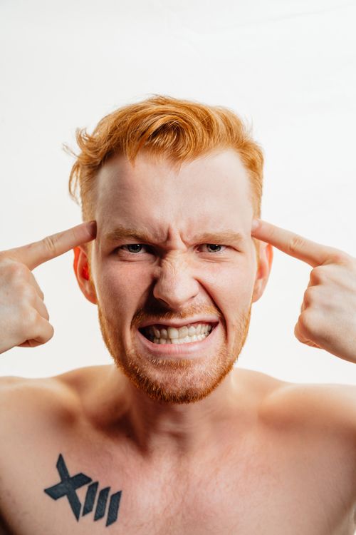 Un uomo con tatuaggi che indica le proprie tempie con un'espressione di rabbia intensa: immagine che rappresenta il legame tra rabbia e meccanismi cerebrali
